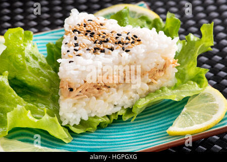 Close up view of Onighiri sushi served with lettuce an lemon on blue plate on black background Stock Photo