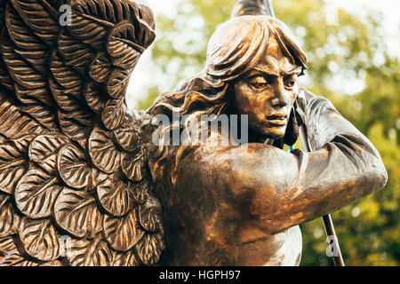 Close Up Detail Of Statue Of Archangel Michael With Outstretched Wings, Thrusting Spear Into Dragon Before Red Catholic Church Of St. Simon And St. He Stock Photo