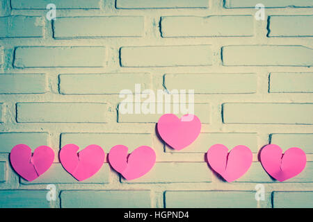 Pink sticky notes broken hearts shaped lined holes on the wall and a heart the outstanding one. vintage style Stock Photo