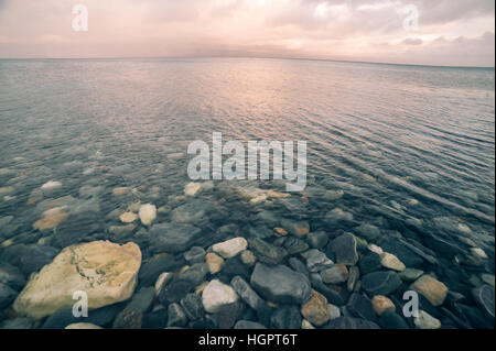 Peaceful view of shallow pristine sea with stones in the bottom and empty horizon at sunset Stock Photo