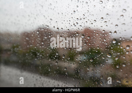 Raindrops on a window glass of a dwelling, where part of the city is seen in the background Stock Photo