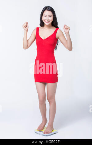 Young smiling woman in red dress standing on a scale cheering Stock Photo