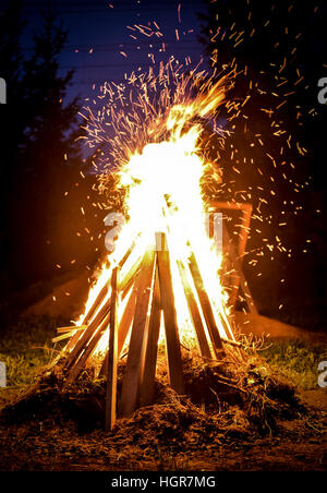Big bonfire and sparks in the night. Orange fire is reaching for the sky. Forrest and trees in the background Stock Photo