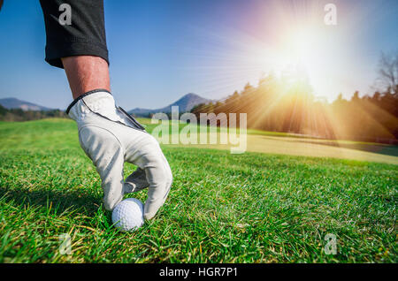 Hand with a glove is placing a golf ball on the ground. Stock Photo