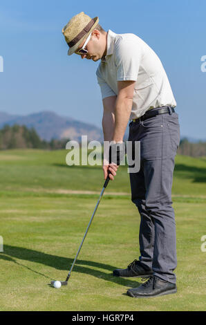 Golfer hitting golf shot with club on course putting on green while on vacation. Golfer is chipping a golf ball onto the green with driver golf club Stock Photo