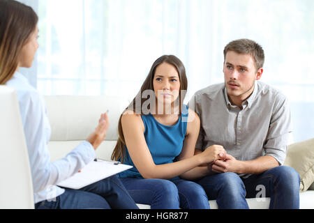 Worried couple listening to marriage counselor during a therapy sitting on a sofa at home Stock Photo