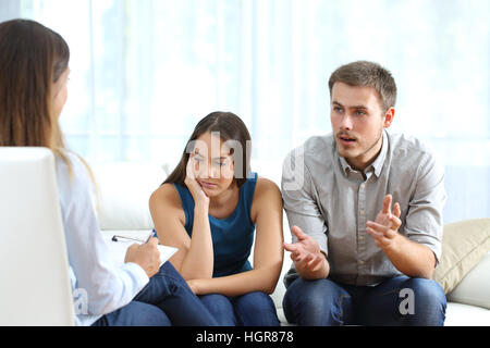 Angry husband and sad wife talking with a marriage counselor before breaking up sitting on a sofa at home Stock Photo