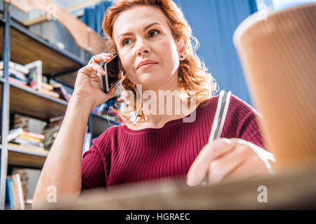 Attractive woman talking on smartphone and holding pen Stock Photo