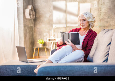 Senior woman sitting on sofa and making notes in notebook Stock Photo