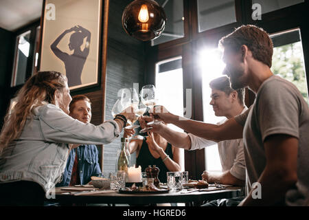 Young man and woman sitting at table and toasting drinks at restaurant. Group of friends toasting wine at cafe. Stock Photo