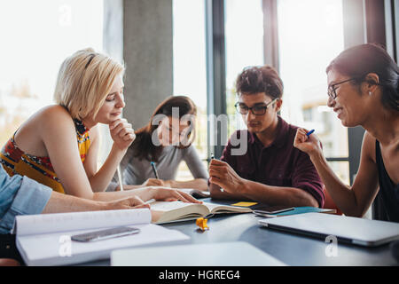 Young people sitting together at table working on school assignment. Diverse group of students studying in a library. Stock Photo
