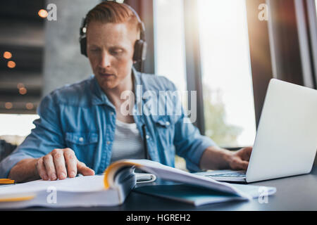 Male student sitting at table with books and laptop. Young man studying in library reading book. Stock Photo