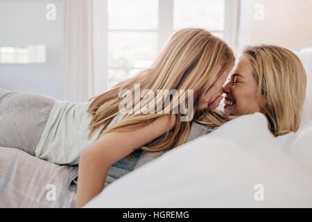 Side view shot of smiling young woman with her daughter in bed. Mother and daughter playing in bedroom and smiling. Stock Photo