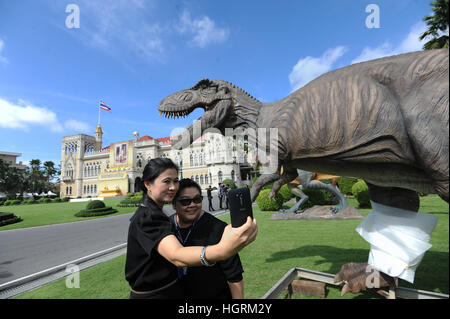Bangkok, Thailand. 12th Jan, 2017. Two staff members pose for a selfie with a dinosaur model in front of the Thai Government House in Bangkok, Thailand, Jan. 12, 2017. Life-size dinosaur models have been temporarily installed on the grounds of the Thai Government House ahead of the Thai Children's Day, when kids and parents are allowed to visit the building complex. © Rachen Sageamsak/Xinhua/Alamy Live News Stock Photo