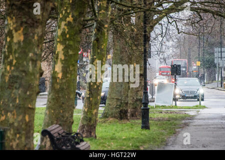 London, UK. 13th Jan, 2017.   Vehicle lights are onin the gloom approaching the Northside - A blizzard of snow sweeps across Clapham Common with an icy Northerly wind. Even so it does not deter dog walkers, joggers and cyclists. © Guy Bell/Alamy Live News 