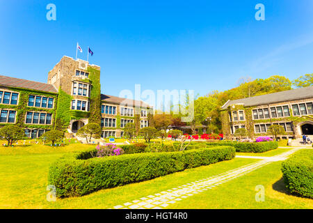 Wide angle view of flags flying over ivy covered main building above grassy quad at Yonsei University in Sinchon, Seoul Stock Photo