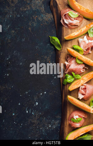 Prosciutto with cantaloupe melon and basil leaves on wooden board Stock Photo