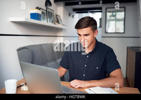 Smiling young man using a laptop at home Stock Photo