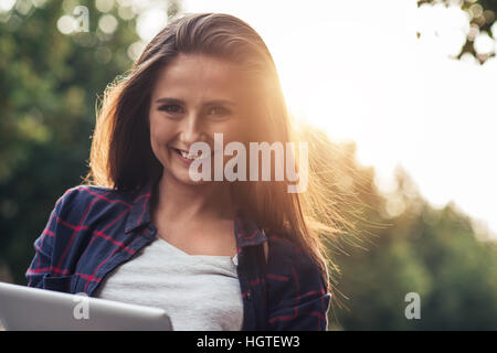 Smiling young woman using a digital tablet outside Stock Photo
