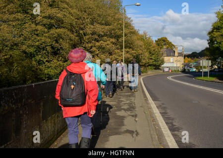 Group of walkers walking along pavement beside road Derbyshire England Stock Photo