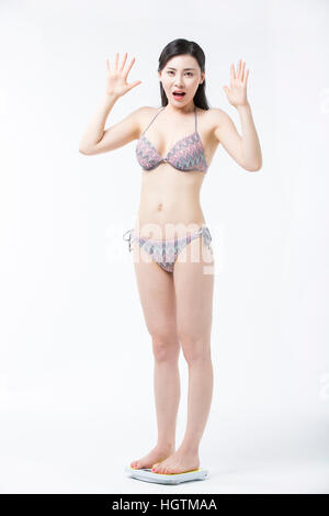 Young woman in bikini standing on a scale surprised Stock Photo