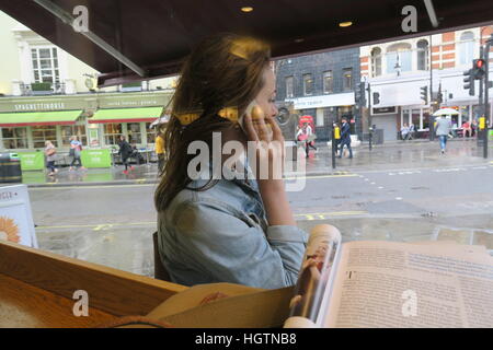 Woman sheltering from rain and using her mobile phone outside restaurant on a London street England
