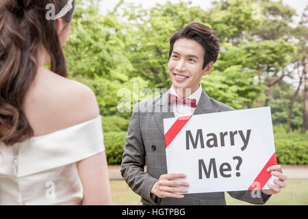 Portrait of young smiling broom holding English message looking at his bride outdoors Stock Photo