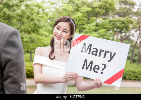 Portrait of young smiling bride showing English message to groom outdoors Stock Photo