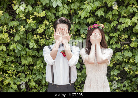 Young couple covering their faces with their hands for wedding photo outdoors Stock Photo