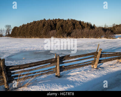 Sun Over Snow covered field with cedar fence in winter Stock Photo