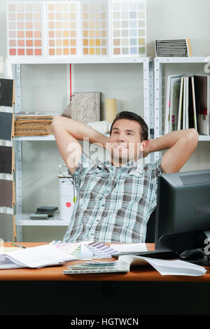 Man sat at desk, leaning back hands behind his head Stock Photo