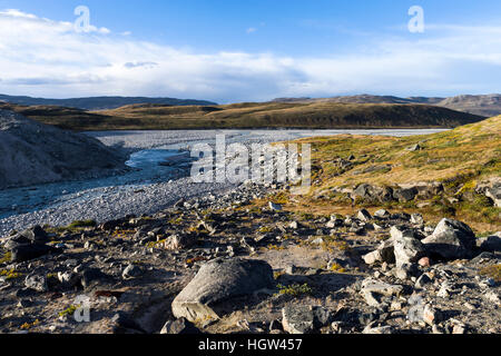 A river flowing along the fracture zone of an enormous glacier across a tundra plain. Stock Photo