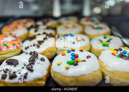 Display of white glazed donuts on tray topped with candy coated chocolate peices and cookies Stock Photo