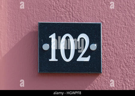 House Number 102 sign on wall painted red Stock Photo