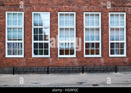 five tall white painted awning windows in a red brick facade facing the street, with a pavement and bicycle stands in front Stock Photo