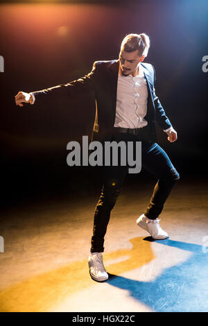 Full length portrait of handsome stylish man in black suit dancing under spotlights Stock Photo