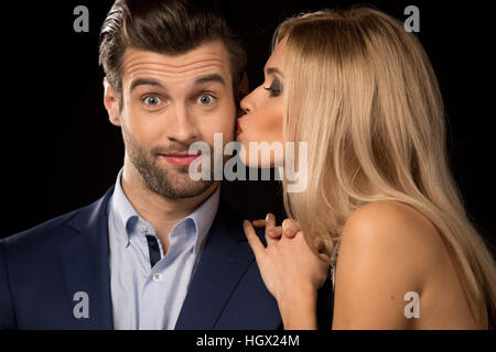 Young woman giving a kiss oh the cheek to happy man on black Stock Photo