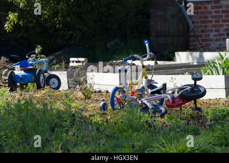 Two children's bicycles and a toy tractor abandoned in a garden Stock Photo