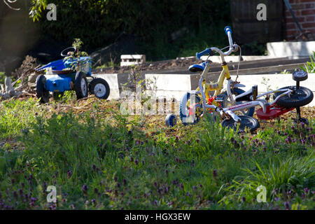 Two children's bicycles and a toy tractor abandoned in a garden Stock Photo