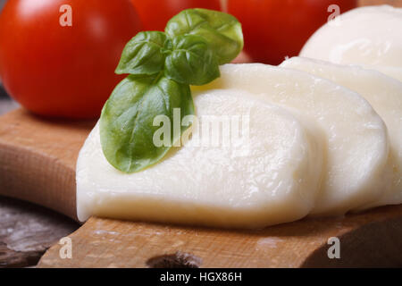 sliced mozzarella on wooden chopping board with green basil. horizontal Stock Photo
