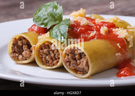 Italian cannelloni pasta with minced meat and tomato sauce on a white plate on the old table. close-up Stock Photo