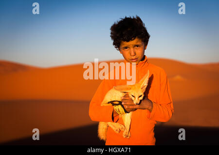Merzouga, Morocco - April 12, 2016: Berber child holding a desert fox poses in the Erg Chebbi dunes in Morocco. Stock Photo