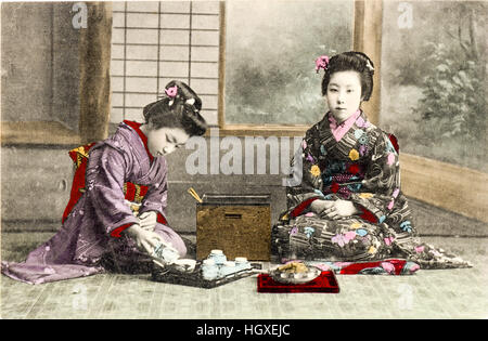 Japan, Vintage postcard hand coloured. Two Geisha in kimono sitting in room conducting tea-ceremony, one pouring tea from kettle. Stock Photo