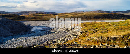 A river flowing along the fracture zone of an enormous glacier across a tundra plain. Stock Photo