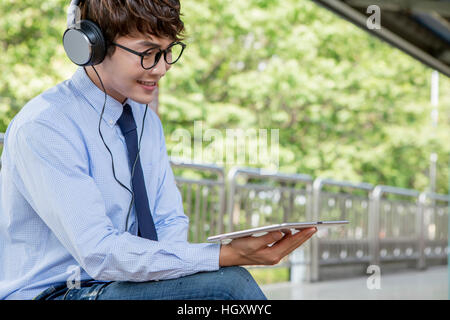 Smiling businessman with headphones using tablet outdoors Stock Photo