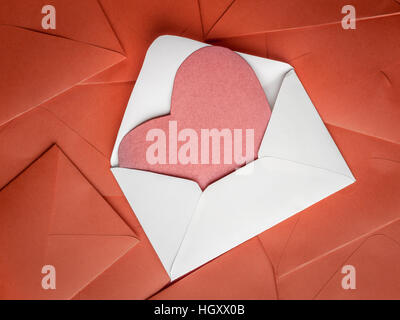White envelope with red paper heart insert placed on pile of red envelopes Stock Photo