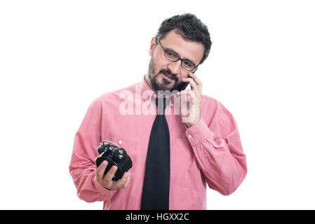 Smiling man with alarm clock talking at his smart phone Stock Photo