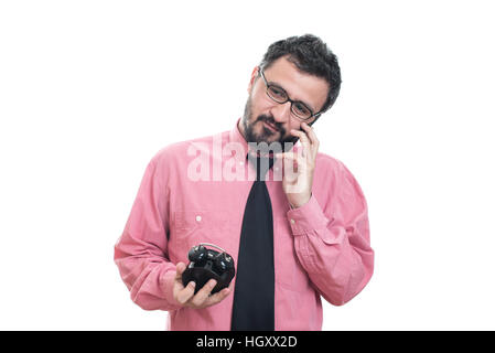 Smiling man with alarm clock talking on smart phone Stock Photo