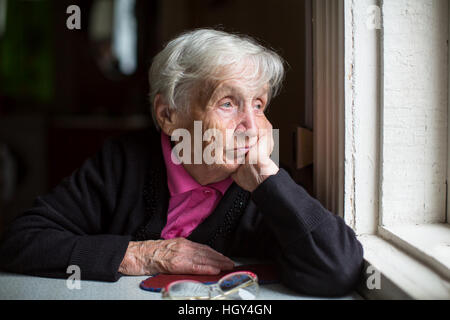 An elderly woman sadly looking out the window. Melancholy and depressed. Stock Photo