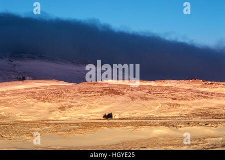 A small house in the sunlight under dark blue clouds in an Icelandic winter landscape Stock Photo